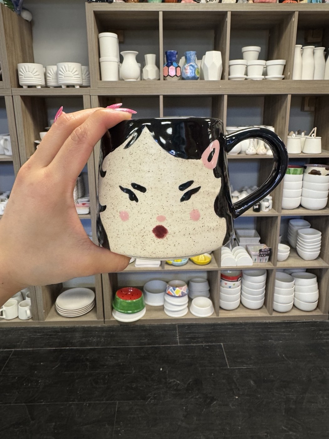 A hand-painted character mug in front of the studio pottery shelves