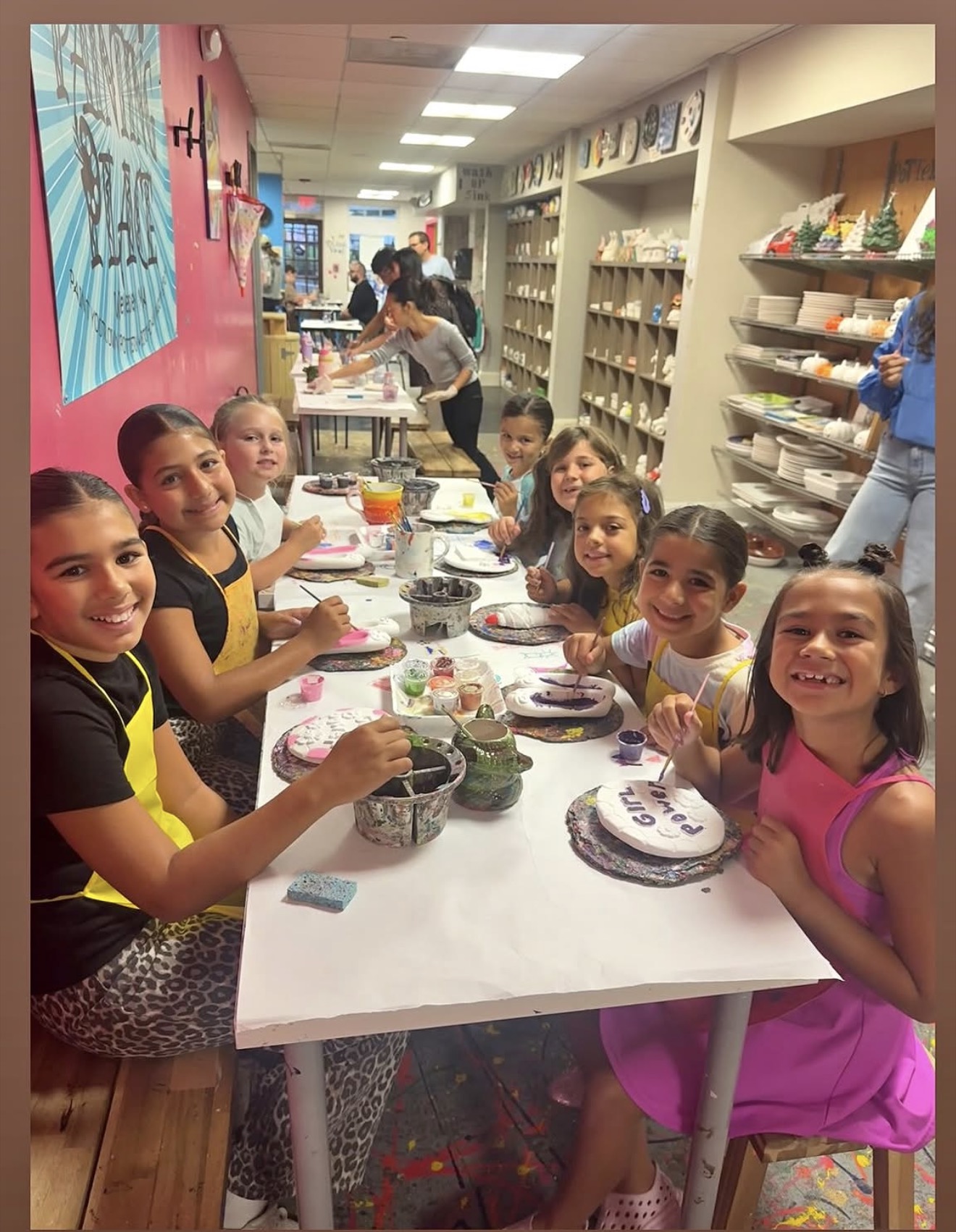 A group of children smiling and painting pottery together at The Painting Place